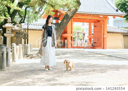 一位面帶微笑的女子牽著她的狗在神社的朱紅色大門前散步。 141293554