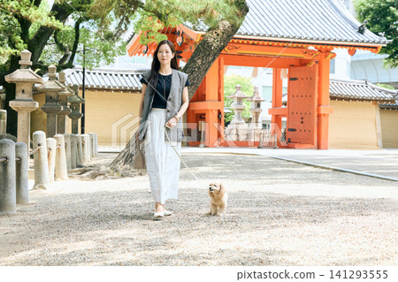 一位女士牽著她的狗在日本寺廟的朱紅色大門前散步。 141293555