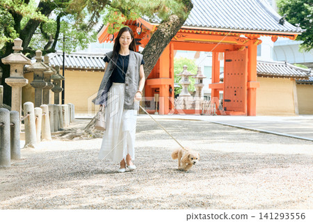 一位年輕女子牽著一隻小狗在日本寺廟前散步。 一位年輕女子牽著一隻小狗在日本寺廟前散步。 141293556