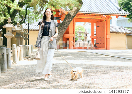 一位面帶微笑的女子牽著她的狗在神社前散步。 一位面帶微笑的女子牽著她的狗在神社前散步。 141293557