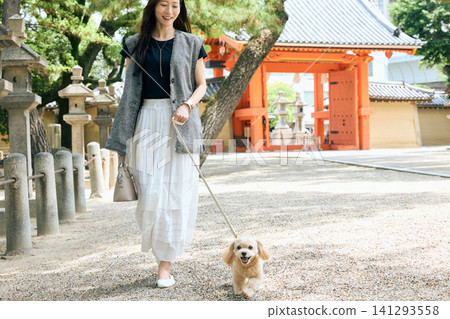A young woman with a smile enjoys walking her dog in the shrine grounds. A young woman with a smile enjoys walking her dog in the shrine grounds. 141293558