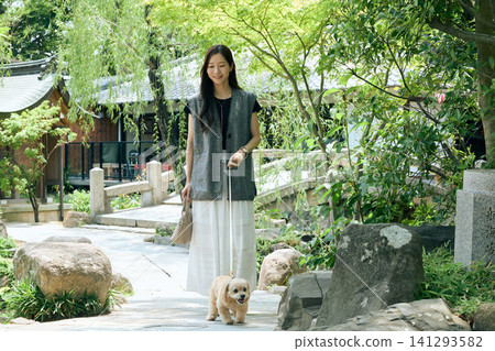 A smiling young woman walking her small dog on a path in a Japanese garden. A smiling young woman walking her small dog on a path in a Japanese garden. 141293582
