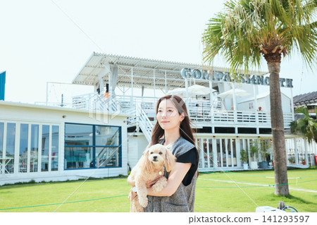 A smiling woman holding her dog in front of a seaside cafe. A smiling woman holding her dog in front of a seaside cafe. 141293597