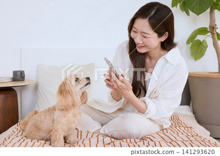 A young woman smiles as she shows her smartphone to her dog while lying in bed. A young woman smiles as she shows her smartphone to her dog while lying in bed. 141293620
