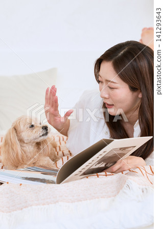 A young woman smiles while reading a magazine in bed with her dog. A young woman smiles while reading a magazine in bed with her dog. 141293643