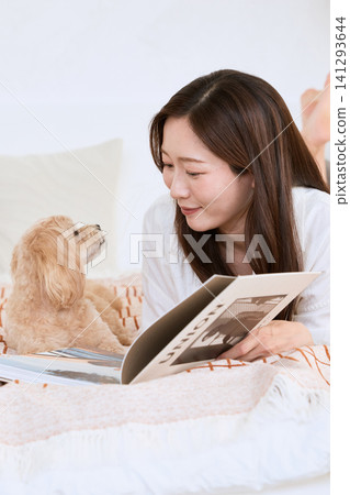 A toy poodle snuggles up to a woman reading a magazine on a sofa. A toy poodle snuggles up to a woman reading a magazine on a sofa. 141293644
