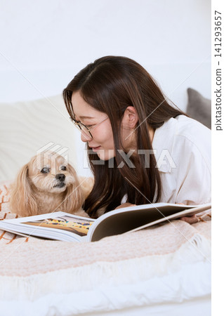 A young woman with glasses reading a magazine in bed with her dog. A young woman with glasses reading a magazine in bed with her dog. 141293657