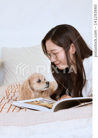 A young woman with glasses reading a magazine on the sofa with her dog. A young woman with glasses reading a magazine on the sofa with her dog. 141293660