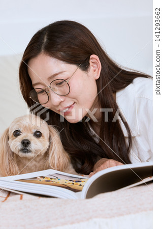 一位戴眼鏡的女士正和她的狗一起看雜誌。 141293662