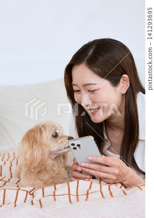A young woman smiles as she relaxes with her dog while looking at her smartphone. A young woman smiles as she relaxes with her dog while looking at her smartphone. 141293695