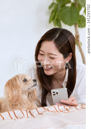 A young woman smiles as she relaxes on the sofa with her dog, looking at her smartphone. A young woman smiles as she relaxes on the sofa with her dog, looking at her smartphone. 141293702