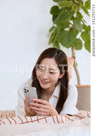 A young woman smiling while looking at her smartphone on the living room sofa. A young woman smiling while looking at her smartphone on the living room sofa. 141293713