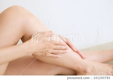 A skincare image of a woman applying body cream to her legs. 141293785
