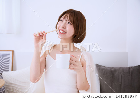 A young woman with a smile brushing her teeth in the living room. A young woman with a smile brushing her teeth in the living room. 141293957