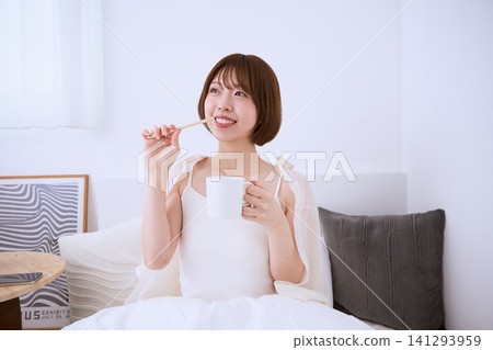 A morning scene of a smiling young woman brushing her teeth in bed. A morning scene of a smiling young woman brushing her teeth in bed. 141293959