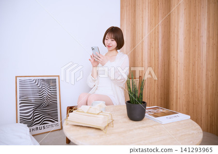 A young woman in white clothes is looking at her smartphone in a stylish room. A young woman in white clothes is looking at her smartphone in a stylish room. 141293965