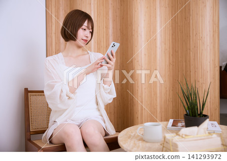 一位留著波波頭的年輕女子正在咖啡館使用智慧型手機。 一位留著波波頭的年輕女子正在咖啡館使用智慧型手機。 141293972