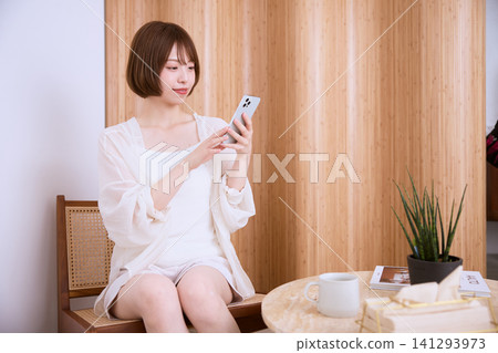 一位留著波波頭的年輕女子在家中使用智慧型手機。 一位留著波波頭的年輕女子在家中使用智慧型手機。 141293973