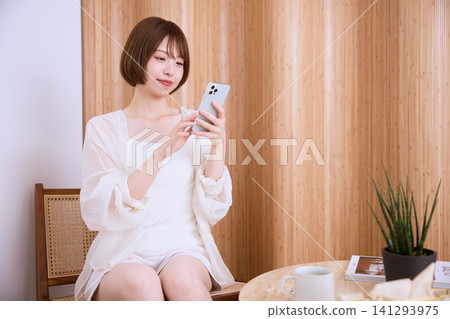 一位留著短髮的年輕女子正在咖啡館使用智慧型手機。 一位留著短髮的年輕女子正在咖啡館使用智慧型手機。 141293975