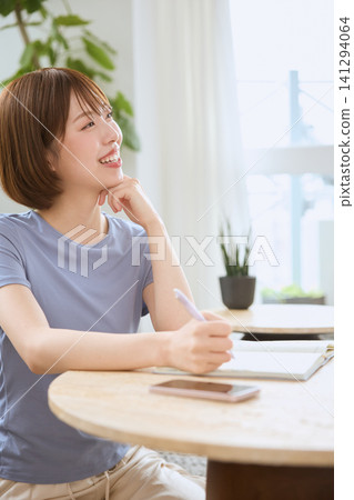 一位年輕女子麵帶微笑,看著客廳裡的平板電腦。 一位年輕女子麵帶微笑,看著客廳裡的平板電腦。 141294064