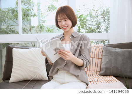 一位留著波波頭的年輕女子坐在沙發上,正津津有味地閱讀。 一位留著波波頭的年輕女子坐在沙發上,正津津有味地閱讀。 141294066