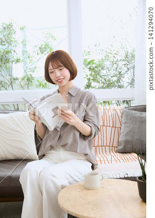 A young woman with a smile reading a book on the living room sofa. A young woman with a smile reading a book on the living room sofa. 141294070