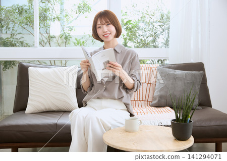 A young woman with a smile reading a book on the living room sofa. A young woman with a smile reading a book on the living room sofa. 141294071