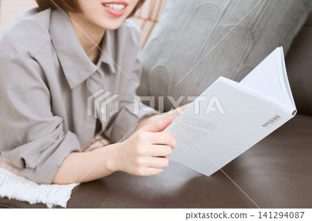 A young woman enjoying reading while relaxing on a sofa. A young woman enjoying reading while relaxing on a sofa. 141294087