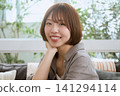 一位留著波波頭的年輕女子在咖啡館裡,手托著下巴,微笑著。 一位留著波波頭的年輕女子在咖啡館裡,手托著下巴,微笑著。 141294114
