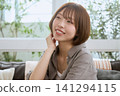 一位留著及耳短髮的年輕女子坐在咖啡館的沙發上,面帶微笑,放鬆地享受著時光。 一位留著及耳短髮的年輕女子坐在咖啡館的沙發上,面帶微笑,放鬆地享受著時光。 141294115