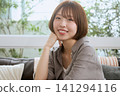 一位留著波波頭的年輕女子麵帶微笑,手托著下巴,坐在咖啡館的沙發上。 一位留著波波頭的年輕女子麵帶微笑,手托著下巴,坐在咖啡館的沙發上。 141294116