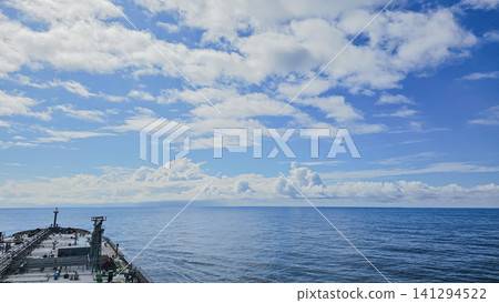 Horizontal high angle view of a large tanker vessel sailing in the calm open ocean under a bright blue sky with scattered fluffy white clouds on a sunny day Horizontal high angle view of a large tanker vessel sailing in the calm open ocean under a bright blue sky with scattered fluffy white clouds on a sunny day 141294522