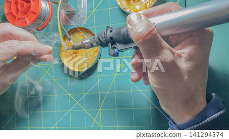Horizontal close up of a person soldering electrical wire with a portable gas blowtorch on a green cutting mat background during a domestic repair project Horizontal close up of a person soldering electrical wire with a portable gas blowtorch on a green cutting mat background during a domestic repair project 141294574