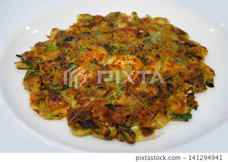 Traditional Korean seafood and green onion pancake served on a white plate, close-up top view. Traditional Korean seafood and green onion pancake served on a white plate, close-up top view. 141294941
