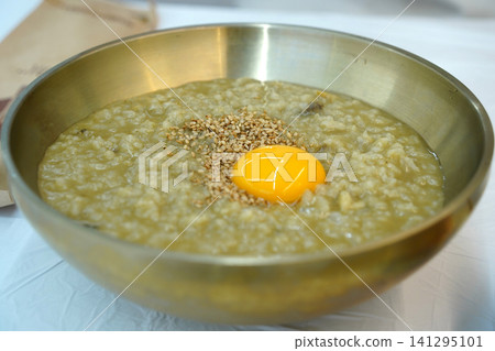Korean abalone porridge topped with raw egg yolk and sesame seeds in a traditional brass bowl. Korean abalone porridge topped with raw egg yolk and sesame seeds in a traditional brass bowl. 141295101