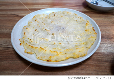 Golden brown and crispy Korean potato pancake on a plate, placed on a wooden table. Golden brown and crispy Korean potato pancake on a plate, placed on a wooden table. 141295244