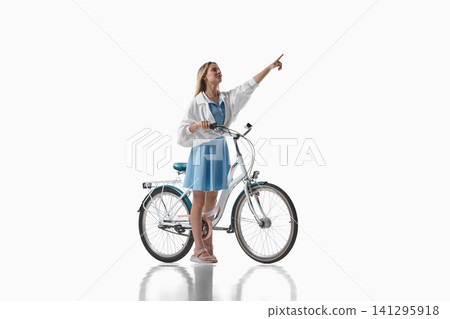 Woman pointing upward beside bicycle on white background Woman pointing upward beside bicycle on white background 141295918