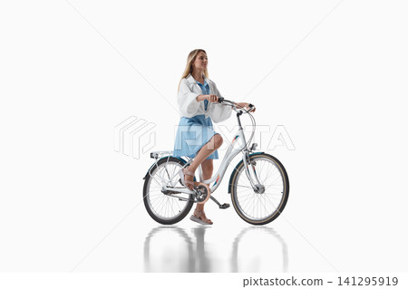 Woman riding city bicycle in white jacket on studio background Woman riding city bicycle in white jacket on studio background 141295919
