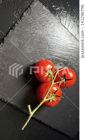 A still-life photograph of a bunch of mini tomatoes placed on a black slate. 141296796