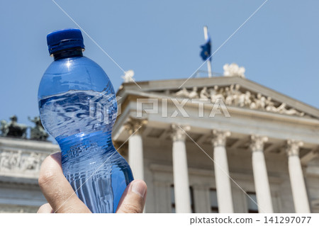 Person holding a plastic water bottle in front of a classical building, symbolizing rising heat and climate change across Europe. Person holding a plastic water bottle in front of a classical building, symbolizing rising heat and climate change across Europe. 141297077
