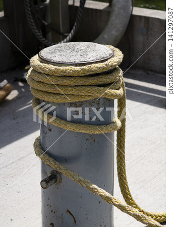 Yellow braided rope wrapped around a mooring bollard at a marina, conveying recreation on the water with a nautical vibe. Yellow braided rope wrapped around a mooring bollard at a marina, conveying recreation on the water with a nautical vibe. 141297087
