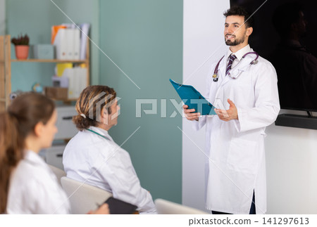 Male doctor holding paper sheets explaining medical topic to students Male doctor holding paper sheets explaining medical topic to students 141297613