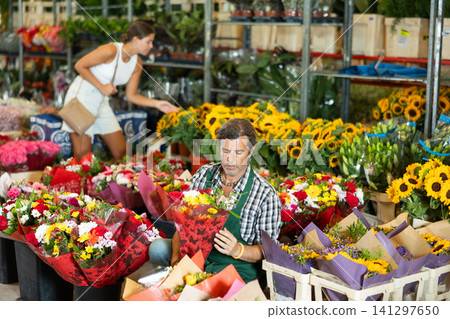 Positive male seller in apron holds designer bouquet in hands Positive male seller in apron holds designer bouquet in hands 141297650