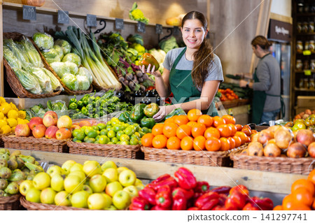 Friendly woman seller laying out ripe bell peppers on a showcase in supermarket 141297741