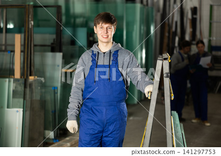 Guy glazer employee in blue overall works in glass processing shop Guy glazer employee in blue overall works in glass processing shop 141297753