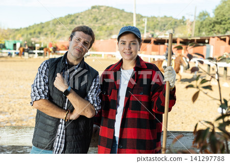 Portrait of skilled male female stable workers in plaid shirts holding working tool rake or pitchfork during work in horse club Portrait of skilled male female stable workers in plaid shirts holding working tool rake or pitchfork during work in horse club 141297788