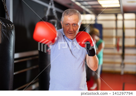 Senior man in boxing gloves posing in fighting stance at gym 141297794