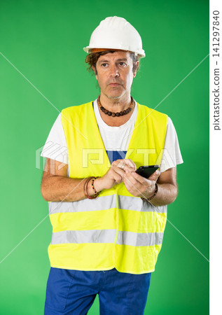 Adult man in reflective vest and hard hat using smartphone for inventory on green screen Adult man in reflective vest and hard hat using smartphone for inventory on green screen 141297840