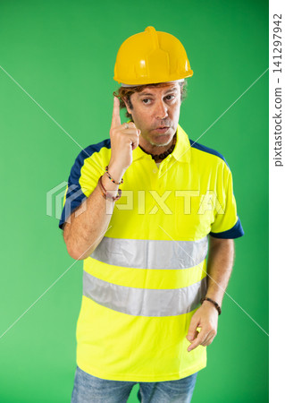 Man in reflective polo and hard hat on green background speaks imaginary partner. Man in reflective polo and hard hat on green background speaks imaginary partner. 141297942
