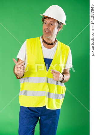 Man in a helmet and overalls stands against the background of a chromakey Man in a helmet and overalls stands against the background of a chromakey 141297949